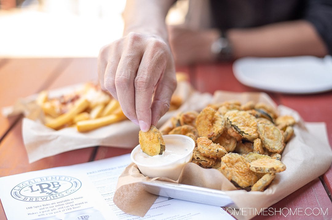 A man's hand dipping a fried pickle chip into dressing at Legal Remedy Brewing in Rock Hill, SC.