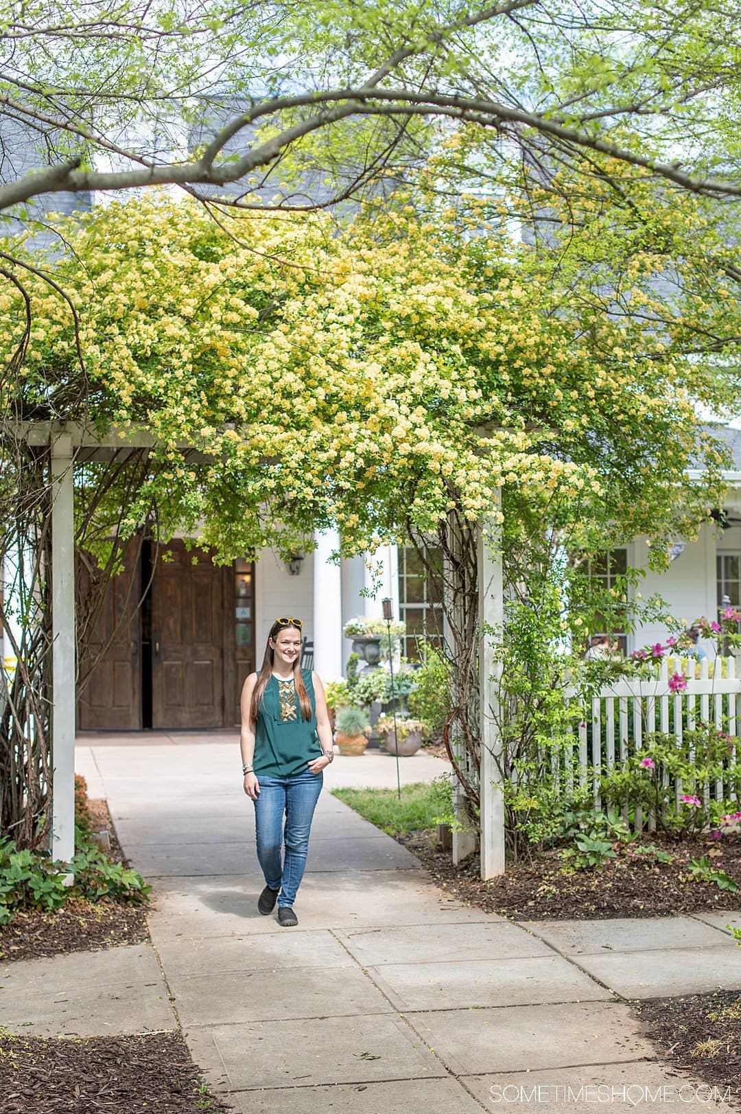 Woman underneath an arch covered by greenery and yellow flowers by Fish Market at Baxter Village in Fort Mill, SC.