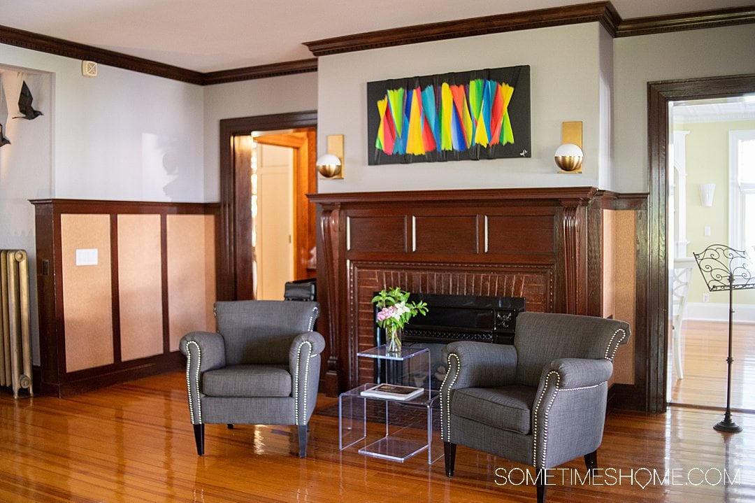 Interior of a modern historical bed and breakfast in Bar Harbor, Maine, with grey chairs and a fluorescent painting above the fireplace.