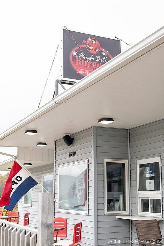 Gray facade of a restaurant with a red, white and blue "open" flag outside.