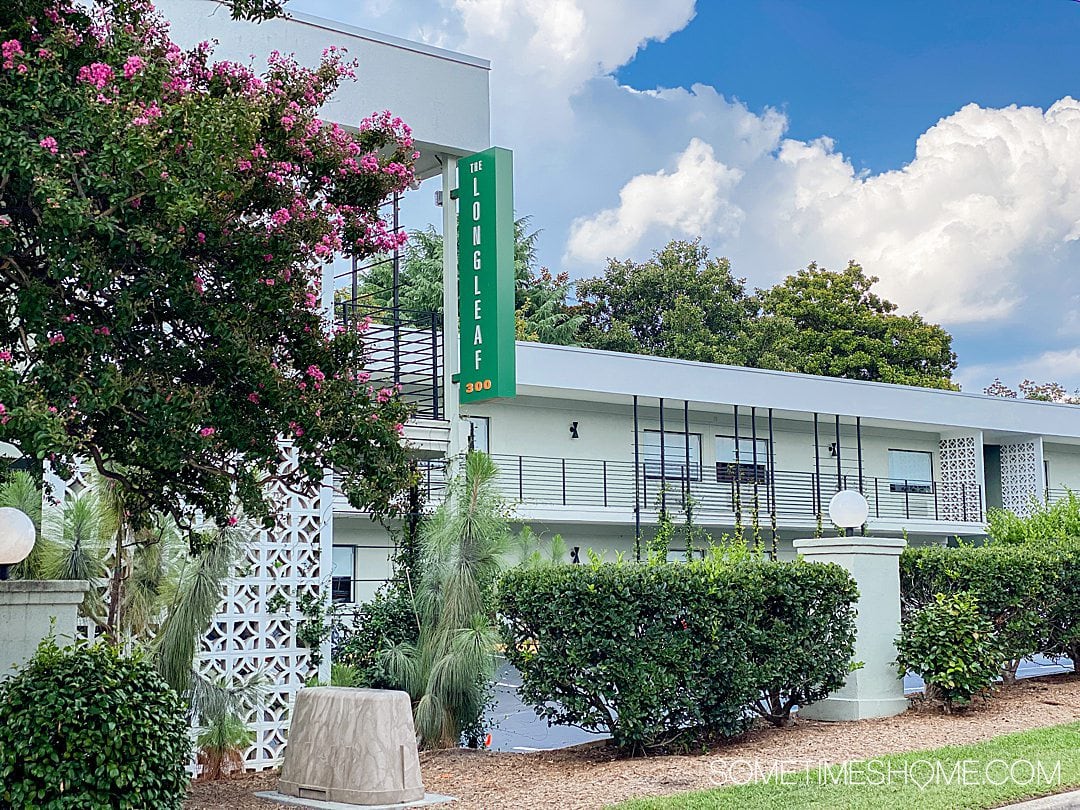 Exterior of a hotel with a Longleaf Hotel sign in green, vertically, and blue skies and green landscaping.