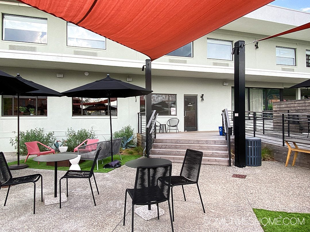 Outdoor area of the Longleaf Hotel, with red-orange shade awnings, black umbrellas and seating areas. 