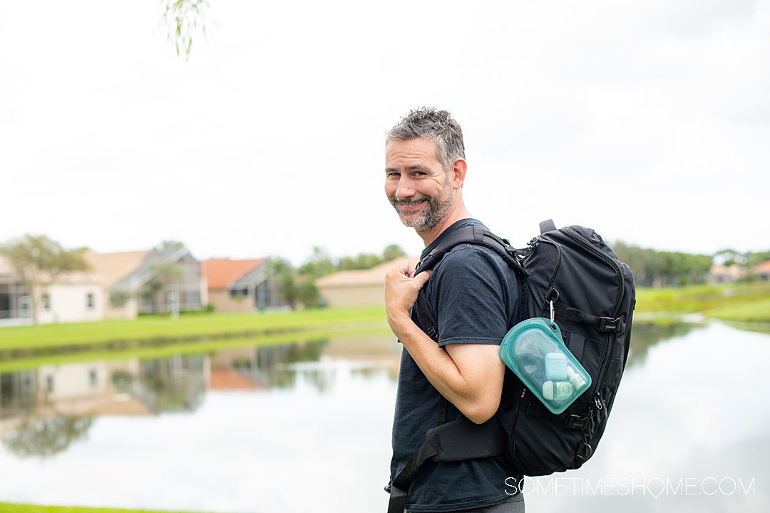 Man with a travel backpack on and a Stasher "Go" bag with a carabiner attached.