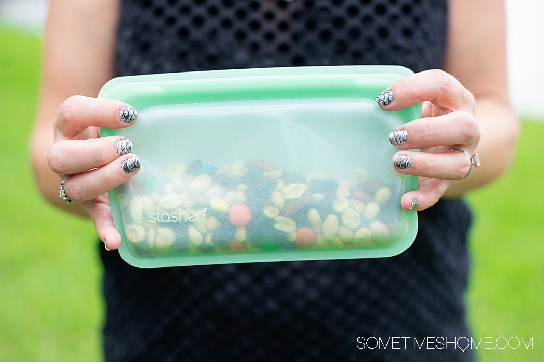 Woman's hands holding a green snack size Stasher bag, a Ziploc bag alternative.