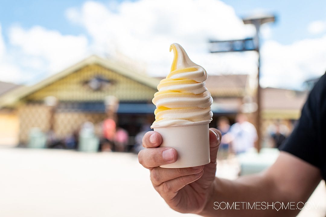 Hand holding a white cup with a Dole Whip and vanilla ice cream swirl.