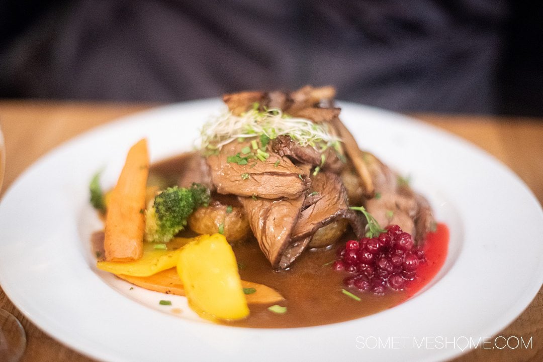 Plate of reindeer meat sliced with potatoes and berries on the side, in a pool of gravy!