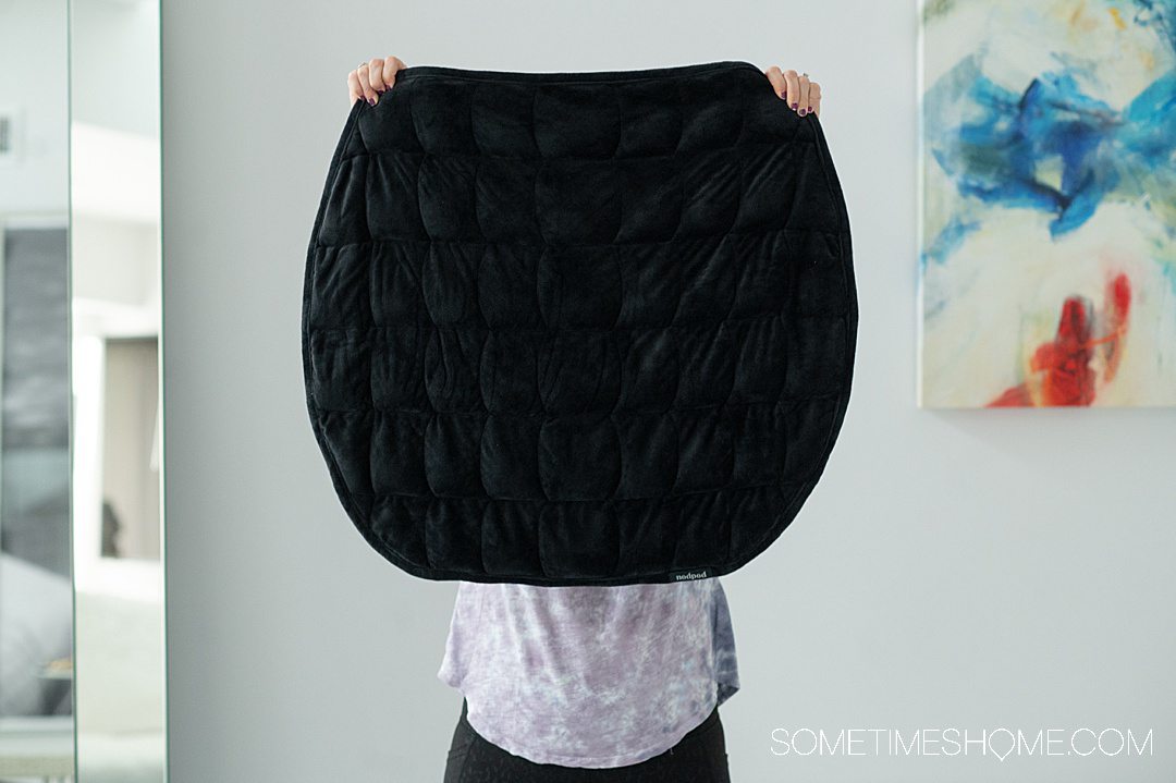 Woman holding up a small black weighted blanket for a review of the nodpod Body.