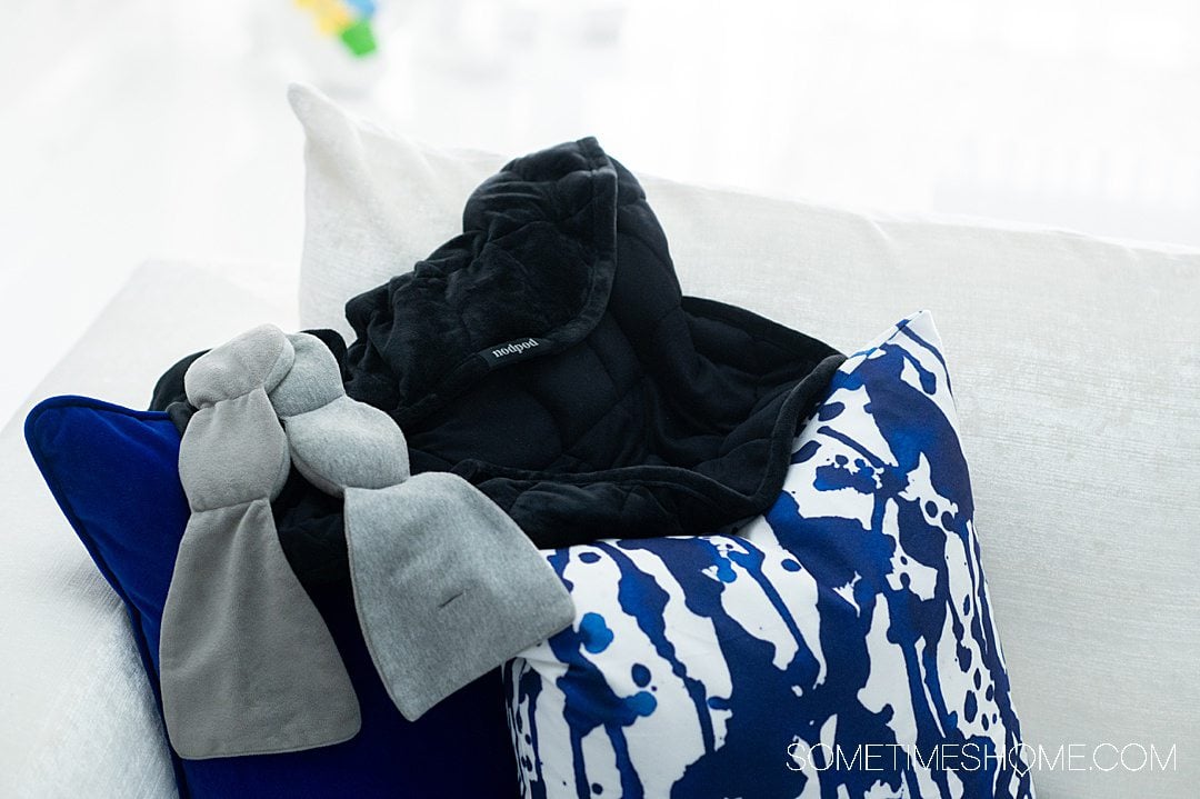 Image of nodpod products: blacked weighted blanket and grey sleep mask, on blue and white pillow.s