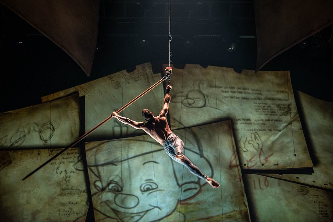 Man suspended in the air during Cirque du Soleil at Disney, Drawn to Life Show, on an oversized pencil. 
