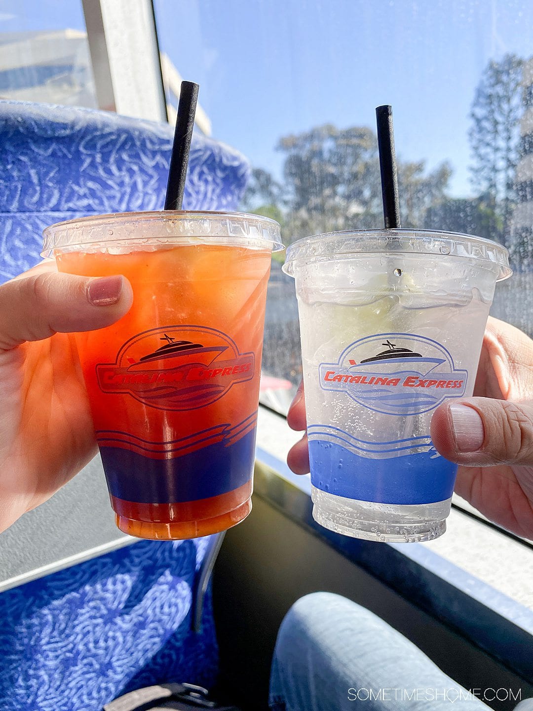 Two hands holding two clear cup drink containers with lids and black straws, aboard Catalina Express on the way to Catalina Island, California.