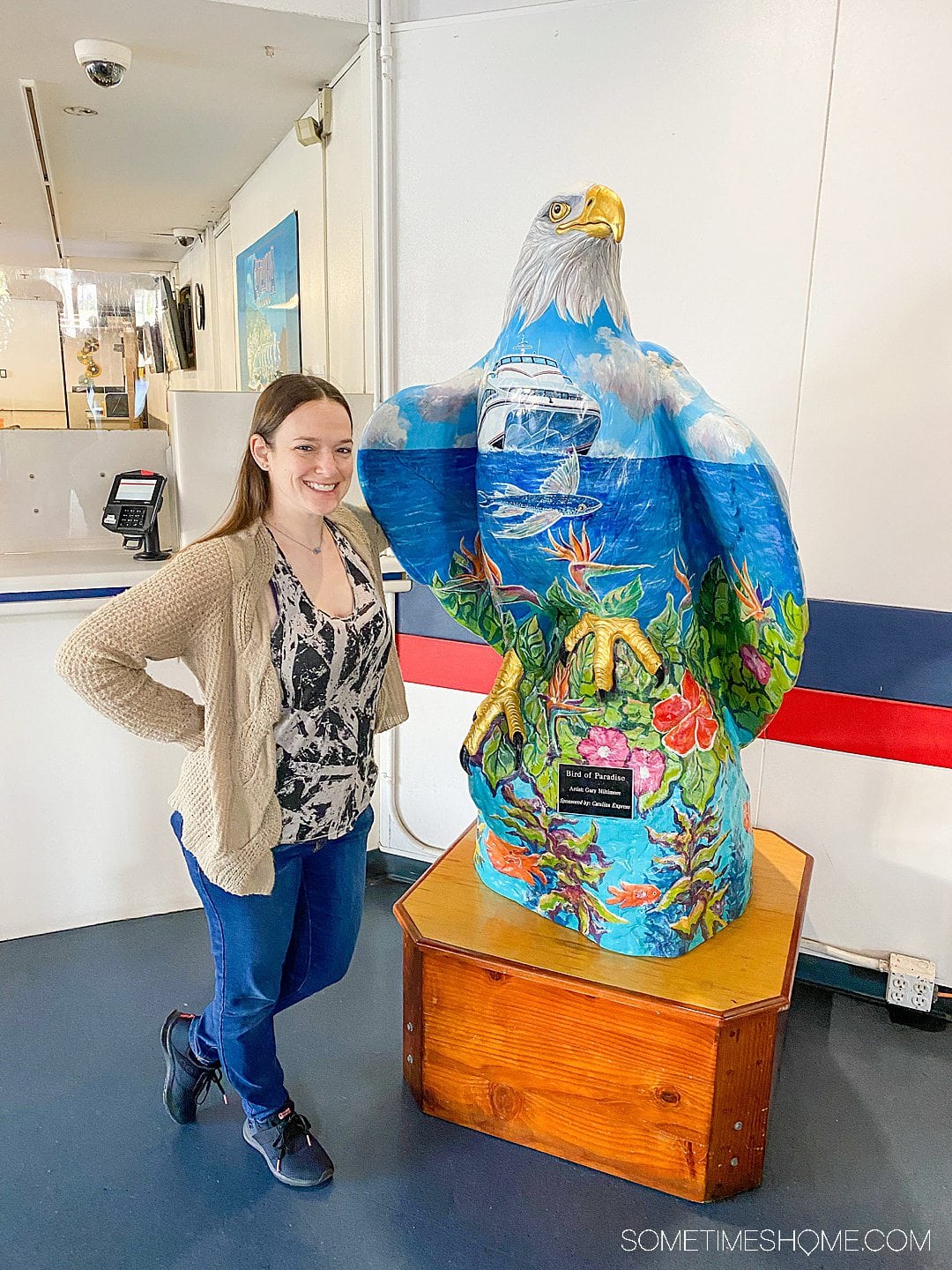Woman standing next to a large sculpture of a bald eagle, colorfully painted with a California scene from Catalina Island.