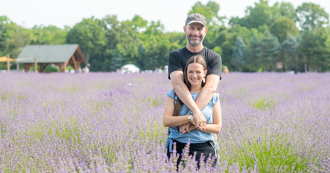 Couple in a lavender field with green trees in the background, for a couples travel website.