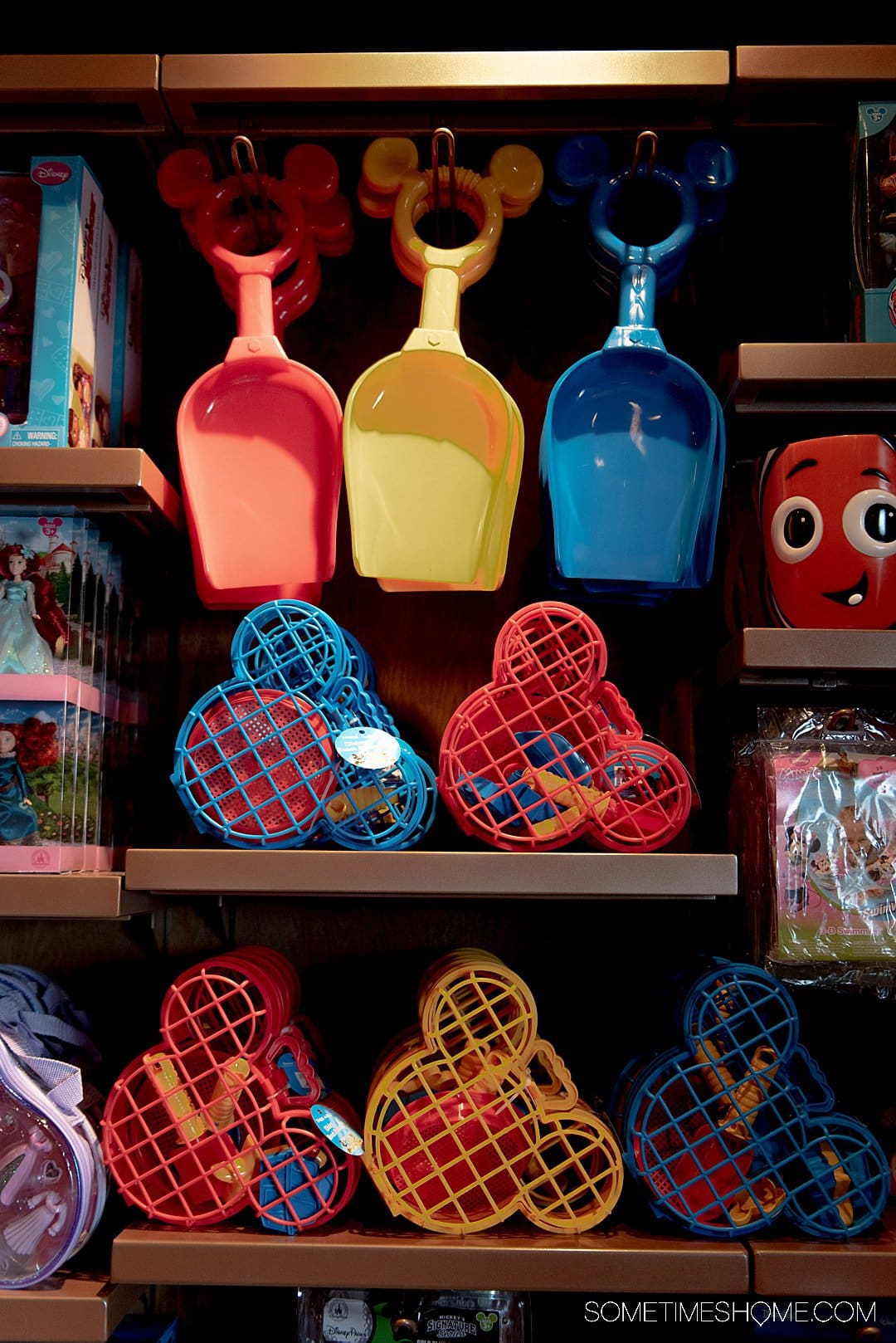 Sand toys on a shelf with Disney motifs and Mickey Mouse, in red, yellow and blue.