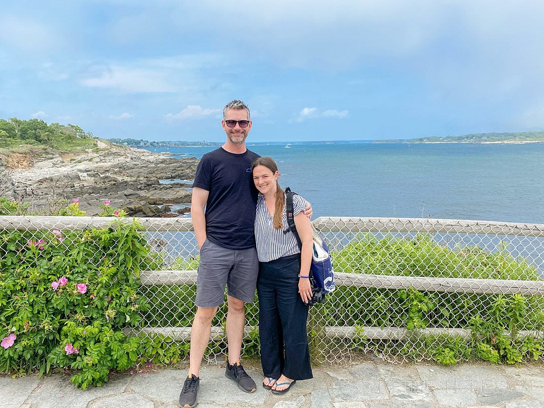 Couple in front of the ocean in Portland, Maine near a lighthouse (not pictured) along the coast.