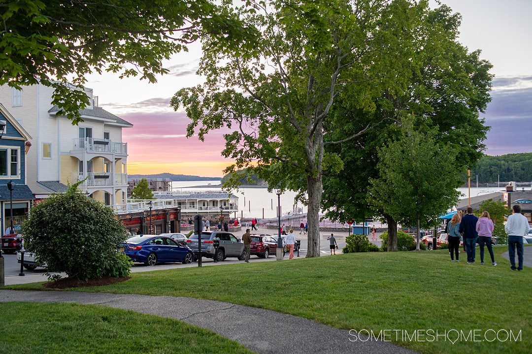 Colorful pink, purple and orange sunset in the town of Bar Harbor, with a green park in the foreground.