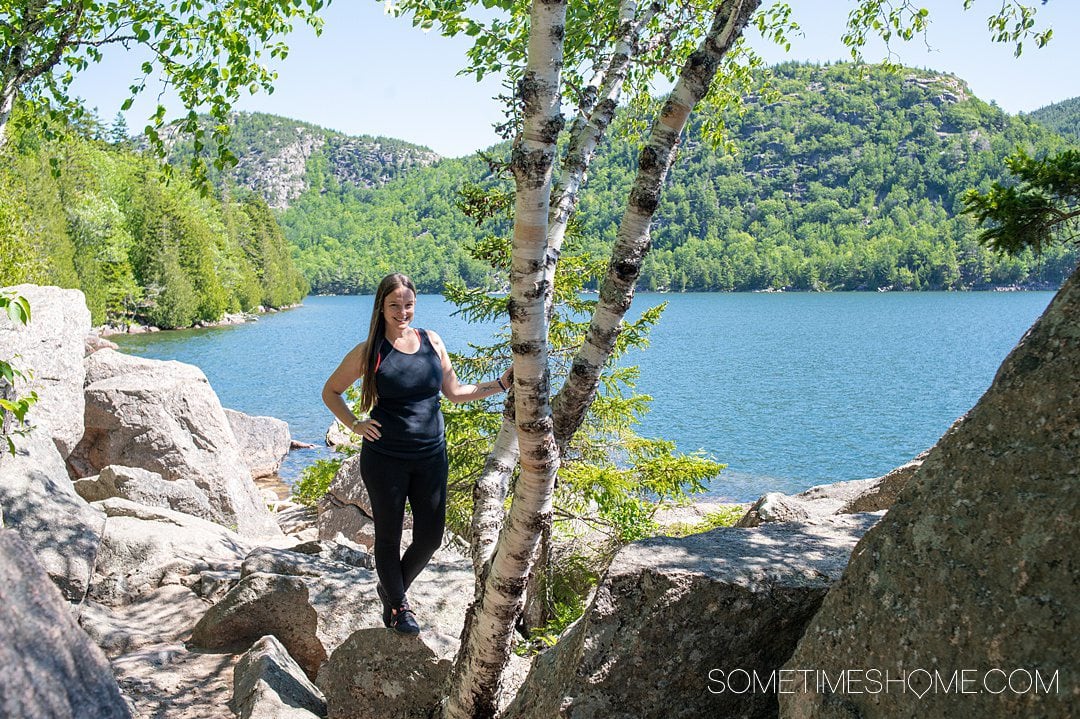 Woman next to a birch tree trunk with a large pond and greenery in the background at Acadia National Park.