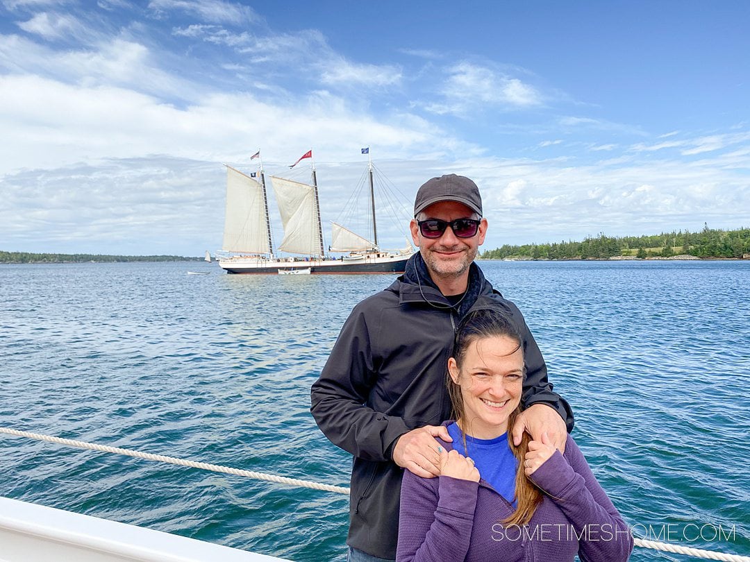 Couple on a ship with a sailboat in the background, part of the Maine Windjammer fleet of boats that sail Maine's coast.