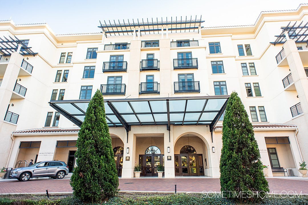 Facade of the Alfond Inn, in Winter Park, with windows and balconies of the hotel room and two tall green trees, for a roundup of the best hotels in Orlando.