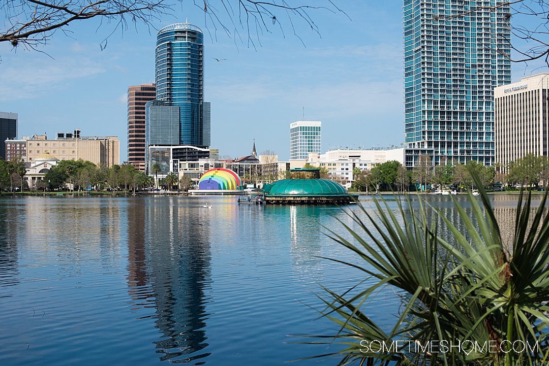 Lake Eola in downtown Orlando with skyscrapers in the distance and a rainbow stage. 