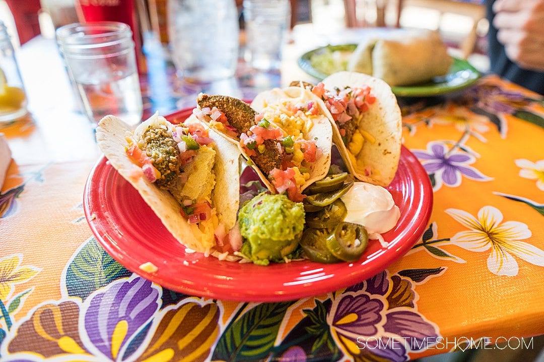 Three tacos on a red plate, on a colorful table.