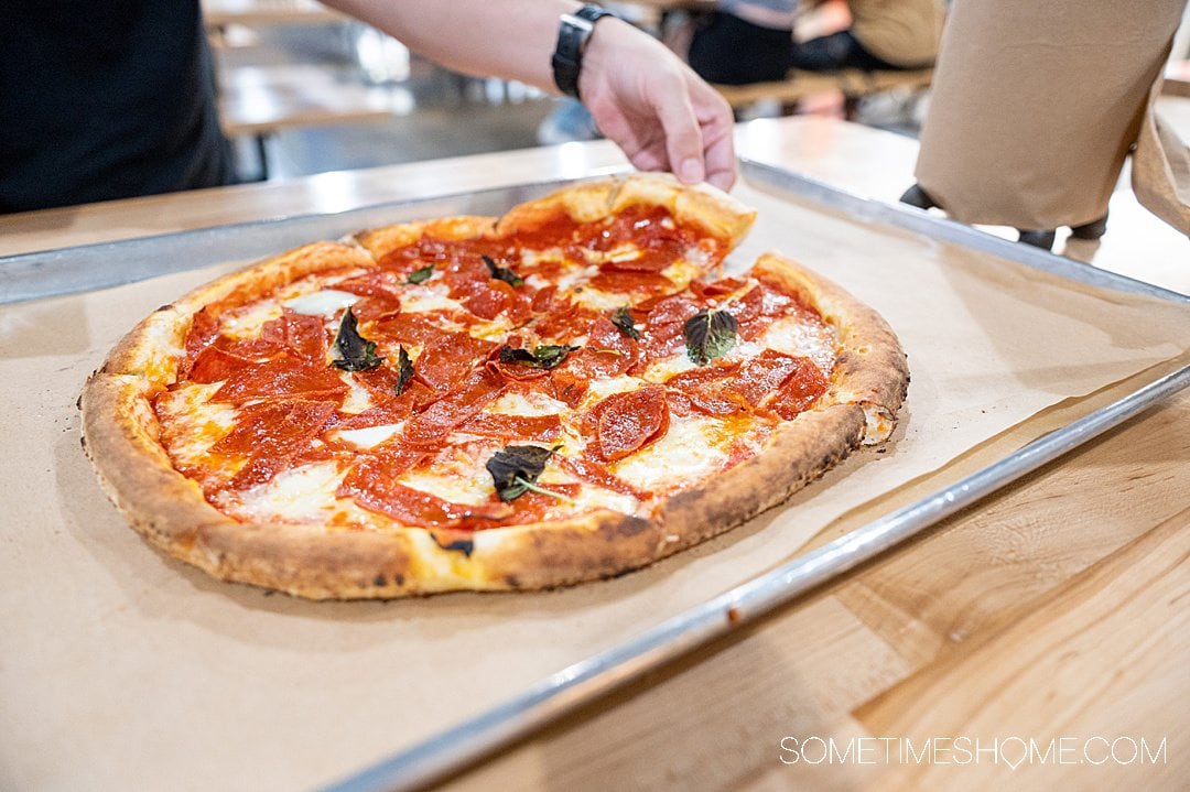 Man's handing pulling a slice of pepperoni pizza off a plate.