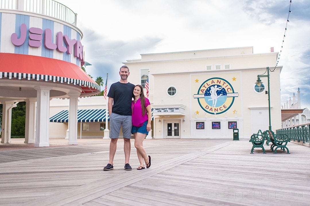 Couple standing in front of Jellyrolls and Atlantic Dance Hall buildings on Disney's Boardwalk at Walt Disney World.