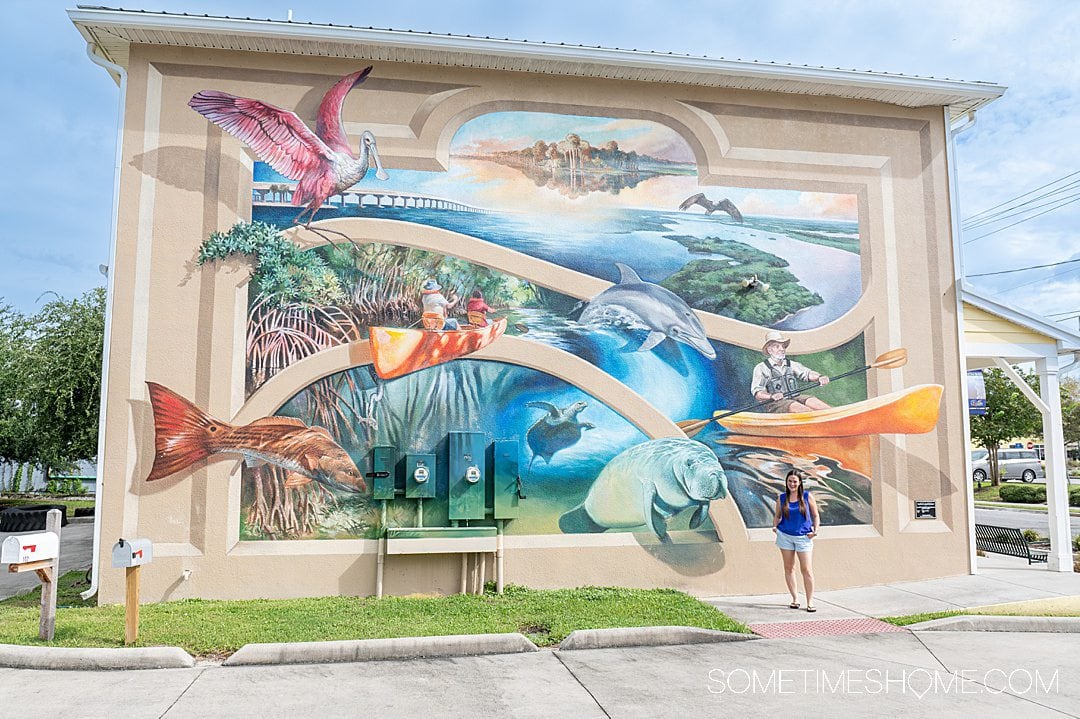 Woman in front of a colorful Florida-themed mural with birds and mammals in Titusville.