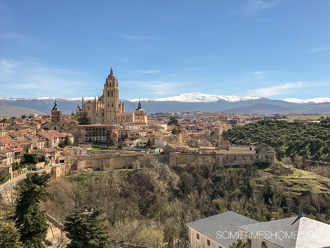 Overview of Segovia, Spain with a castle and snow-capped mountains in the distance.