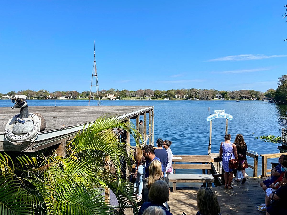 Looking out to the water with a blue sky, and people in line on a dock for a "Scenic Boat Tour" near Orlando, Florida.