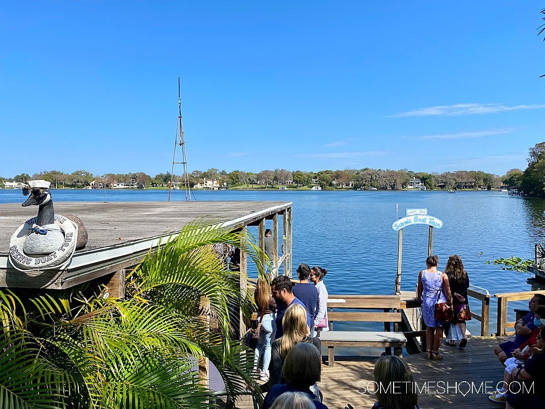 View of the water and a blue sky, with a "Scenic Boat Tour" sign and people waiting for an Orlando Boat Tour.