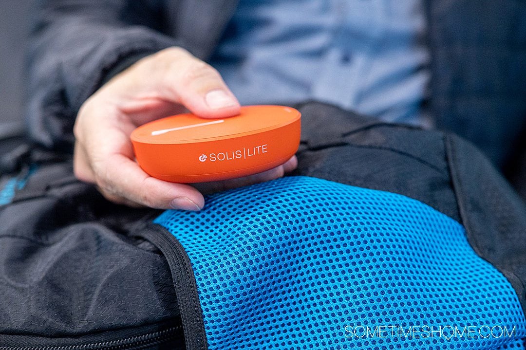 Hand holding a pocket wifi device on a blue and black backpack for a Skyroam Solis Lite review.