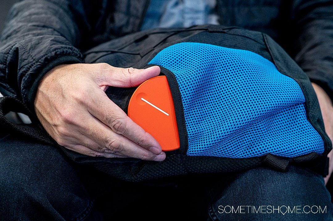 Hand holding a pocket wifi device on a blue and black backpack for a Skyroam Solis Lite review.