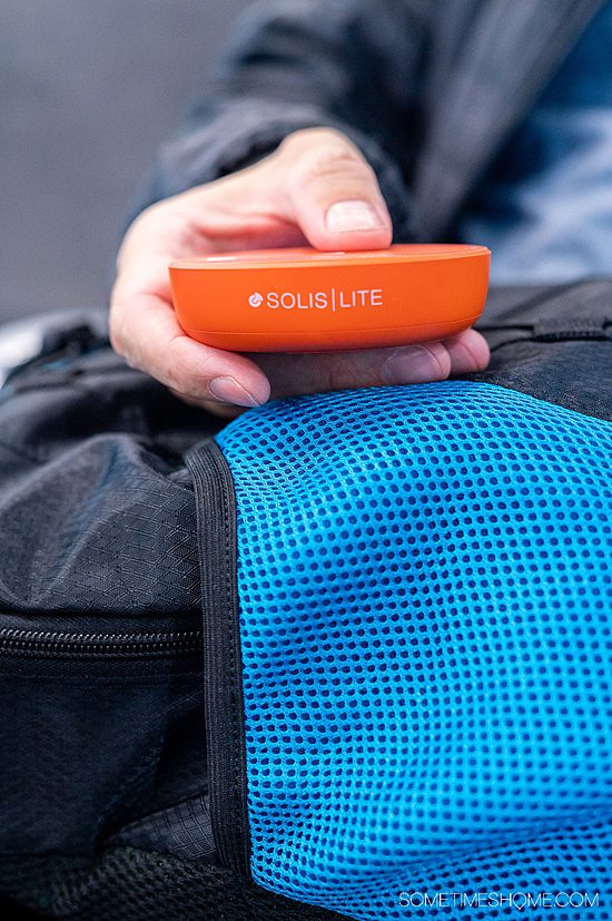 Hand holding a pocket wifi device on a blue and black backpack for a Skyroam Solis Lite review.