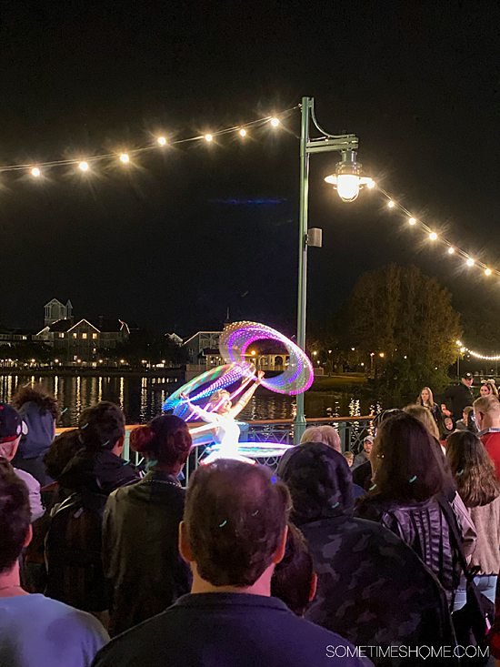 Performers hula-hooping on Disney's BoardWalk at night with an audience in front of them.