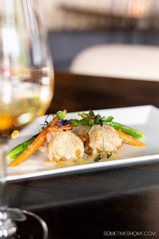 Rectangular plate of food with a white sauce covering two fried shrimp, under a green asparagus and orange carrot.