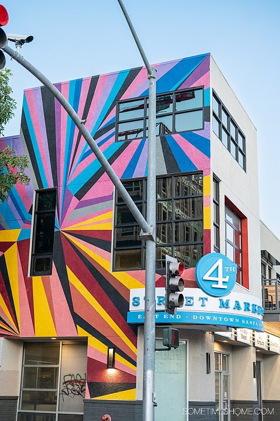 Geometric purple, blue, pink, orange and yellow mural on the side of a building with "4 Street Market" sign in blue on the corner of the building in Santa Ana, California.