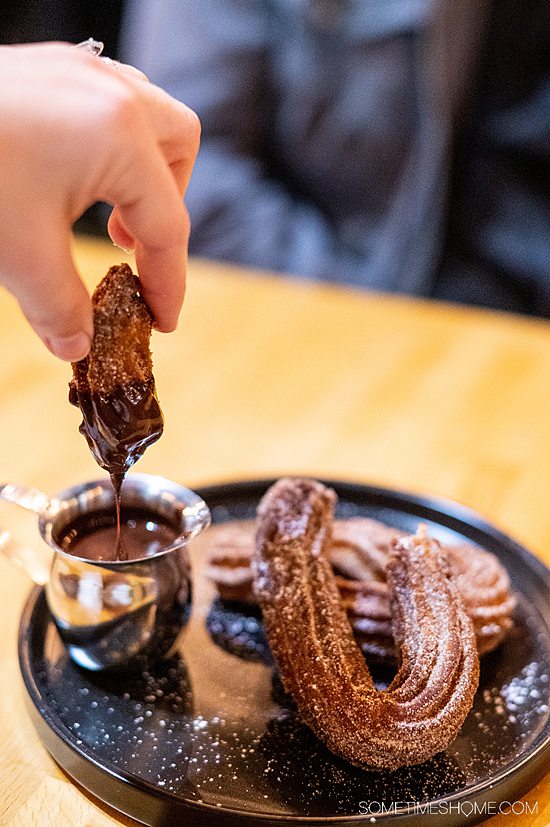 Hand dipping a piece of a churro in melted chocolate at Lola Gaspar in Santa Ana.