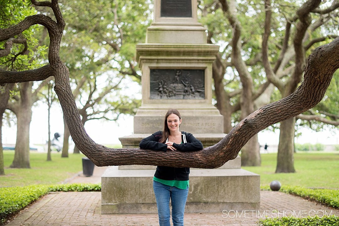 Woman posing on a large branch of a southern oak tree in White Point Park, with a monument behind her in Charleston, SC.