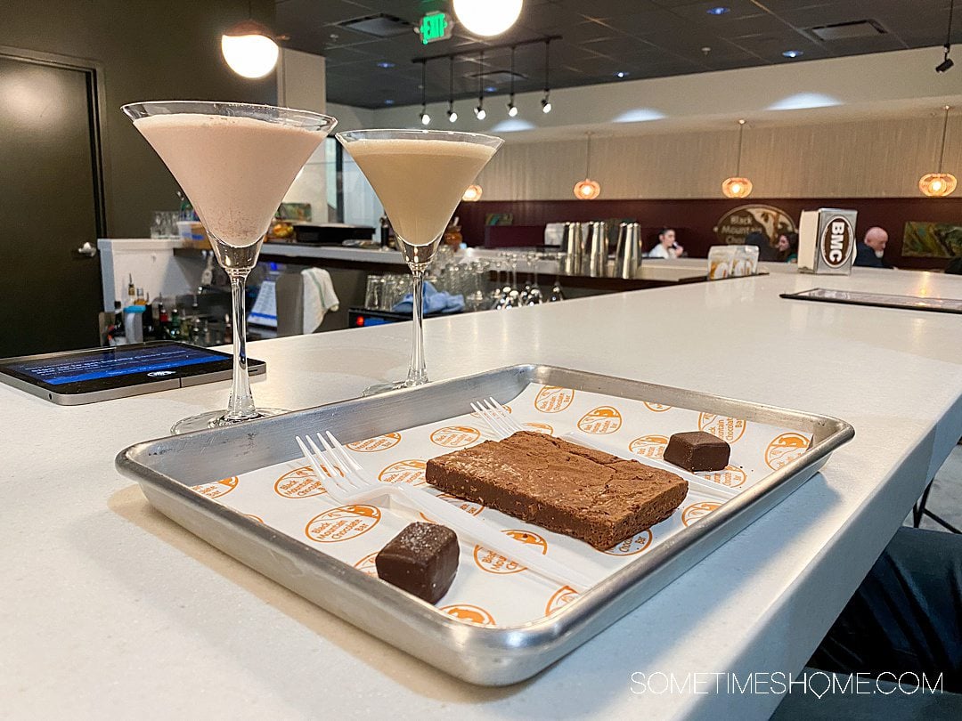 Two martini glasses and a silver tray with chocolates and a brownie on a white counter at Black Mountain Chocolate in Winston-Salem.