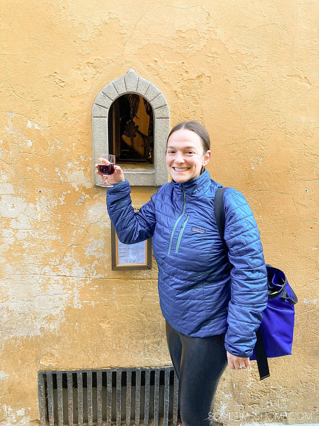 Woman holding a glass of red wine given through a wine window during a food tour in Florence.