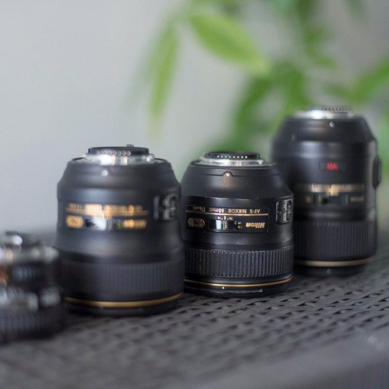 Four black Nikon lenses in a row on a gray shelf.