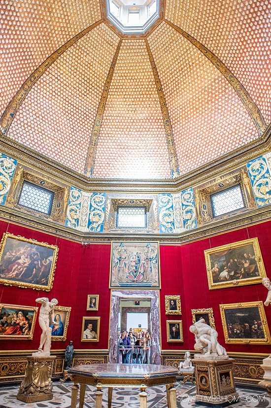 Inside one of the Medici galleries in the Uffizi gallery in Florence, with red walls, gold-framed art and sculptures.
