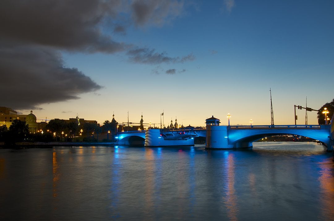 Tampa Bay bridge during dusk with a blue and yellow sky over a blue-lit bridge.