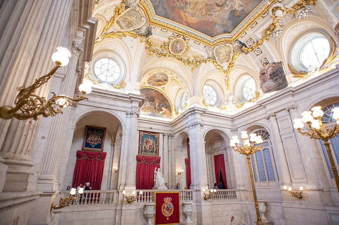 Top of the opulent Grand Staircase at the Royal Palace of Madrid in Spain, with a ceiling painting and gold decoration. 