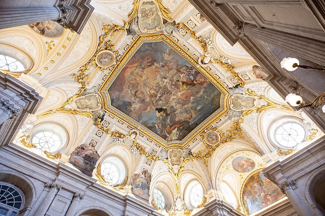 Ceiling painting in the Grand Staircase of the Royal Palace of Madrid surrounded by gold decoration.