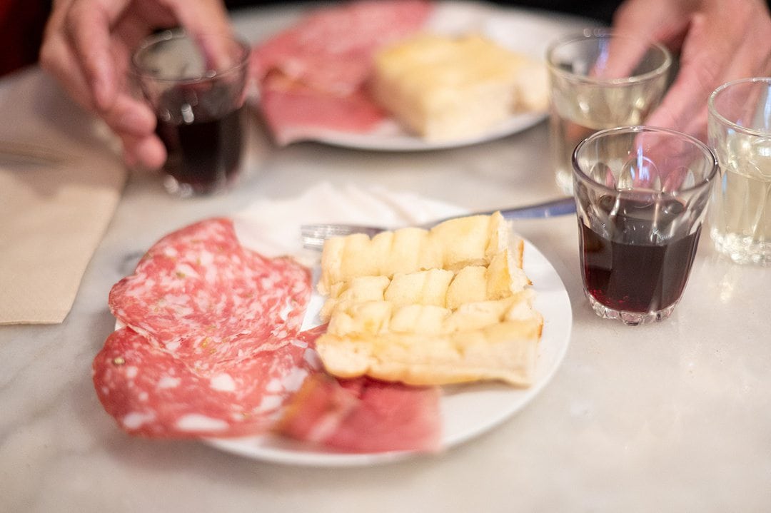 Plate of salami and bread with wine in glass cups.