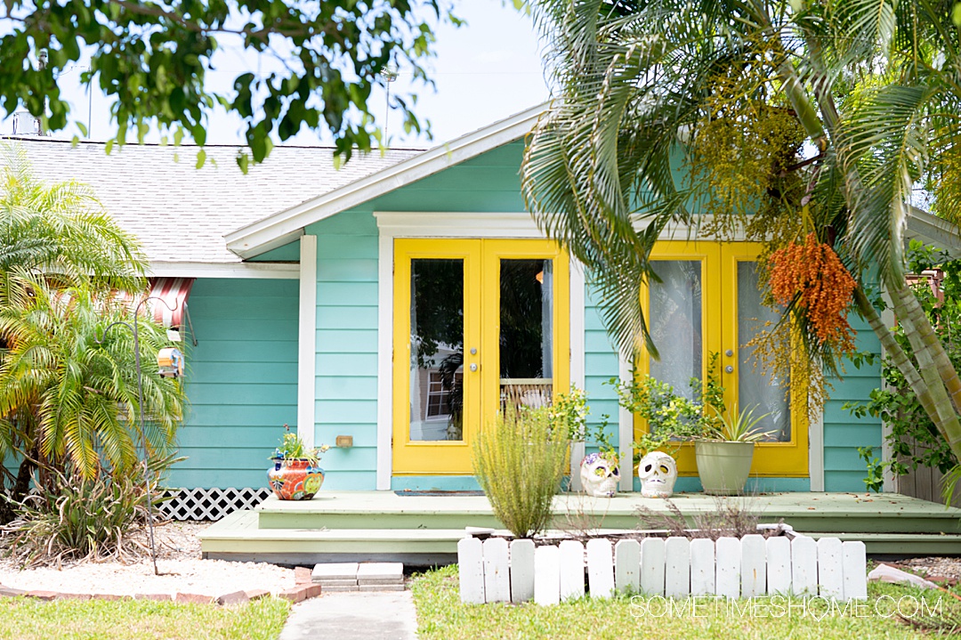 Blue house with yellow-painted doorframes and greenery in the yard.