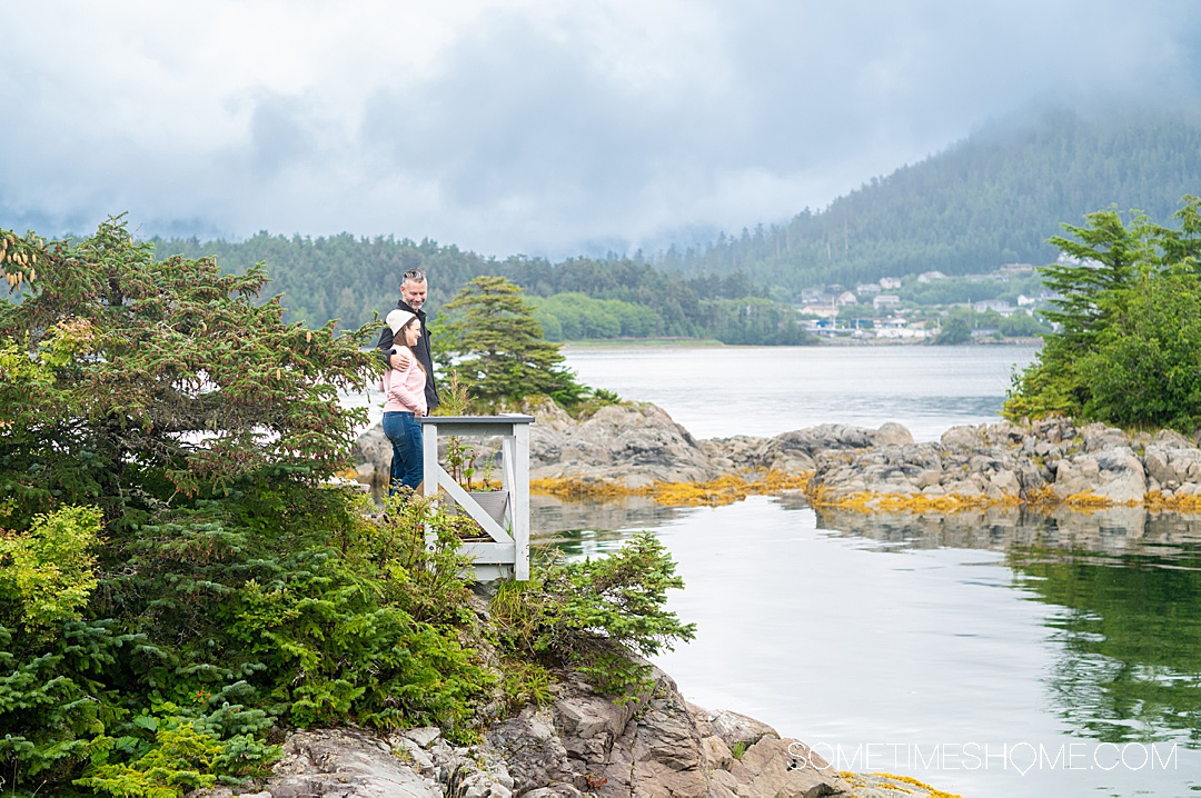 Couple looking out to the ocean from a dock in the distance with mountains and evergreen in Sitka, at an all-inclusive Alaska resort.