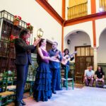 Flamenco dancers lined up on a stage inside a venue with arched architecture details in Seville.
