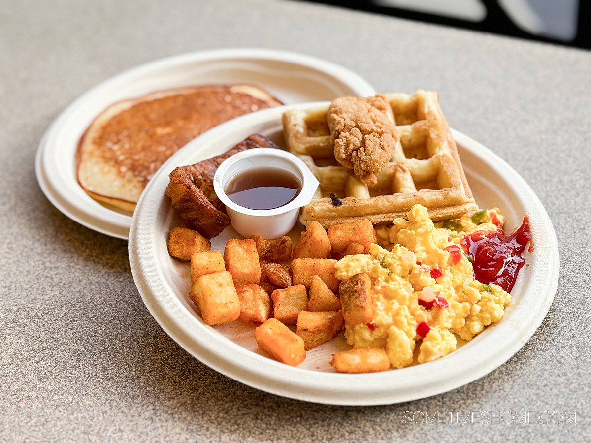Plates of breakfast food at Discovery Cove: waffles, potatoes and eggs, with a small bowl of syrup, and a plate of pancakes behind it.